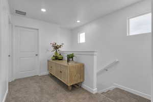 Hallway with an upstairs landing, light carpet, baseboards, visible vents, and recessed lighting