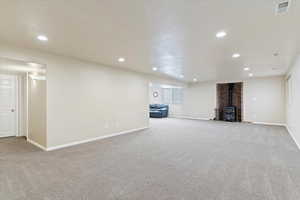 Below grade area featuring visible vents, carpet flooring, recessed lighting, and a wood stove
