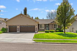 Ranch-style house with driveway, stone siding, an attached garage, a front yard, and stucco siding