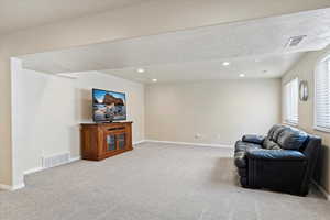 Carpeted living area with baseboards, visible vents, recessed lighting, and a textured ceiling