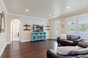 Living room featuring recessed lighting, dark wood-style floors, arched walkways, crown molding, and baseboards