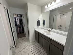 Bathroom with a walk in closet, vanity, marble finish floor, shower / tub combination, and baseboards