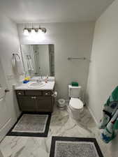 Bathroom with marble finish floor, toilet, vanity, and baseboards