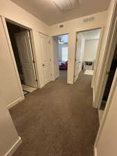Hall with dark carpet, baseboards, and visible vents