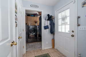 Interior space with washing machine and clothes dryer, cabinet space, light tile patterned flooring, and baseboards