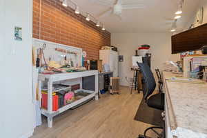 Office featuring a ceiling fan, track lighting, brick wall, a workshop area, and light wood-style flooring