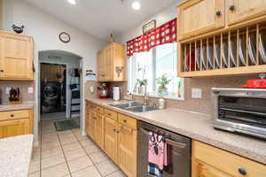 Kitchen featuring stainless steel dishwasher, light brown cabinetry, a sink, washer / clothes dryer, and light countertops