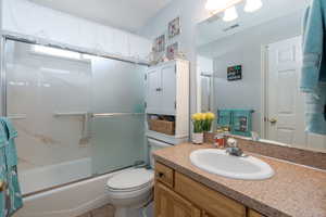 Bathroom featuring visible vents, toilet, enclosed tub / shower combo, and vanity