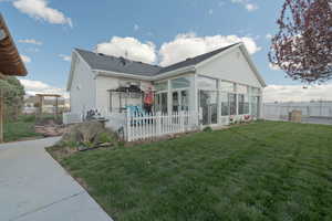 Rear view of house with a lawn, a fenced backyard, a sunroom, and roof with shingles