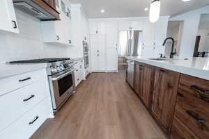 Kitchen with white cabinets, a sink, light wood-type flooring, exhaust hood, and appliances with stainless steel finishes