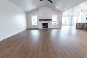Unfurnished living room with ceiling fan with notable chandelier, baseboards, a large fireplace, and lofted ceiling