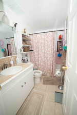 Bathroom featuring tile patterned floors, shower / bath combination with curtain, toilet, vanity, and tasteful backsplash