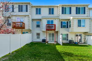 Rear view of property featuring a lawn, central AC, stucco siding, and fence