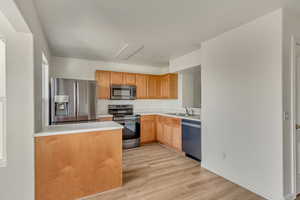 Kitchen with a sink, light wood-type flooring, light countertops, a peninsula, and appliances with stainless steel finishes