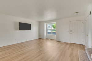 Unfurnished living room featuring light wood finished floors, baseboards, and ornamental molding