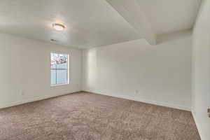 Carpeted empty room featuring baseboards, beam ceiling, and visible vents