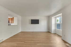 Unfurnished living room featuring light wood finished floors, visible vents, crown molding, and baseboards