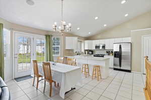 Dining room with vaulted ceiling, light tile patterned flooring, and an inviting chandelier