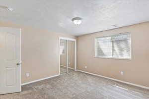 Unfurnished bedroom with a textured ceiling, a closet, carpet, baseboards, and visible vents