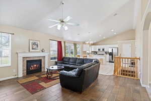 Living area featuring recessed lighting, wood finished floors, a stone fireplace, baseboards, and ceiling fan with notable chandelier