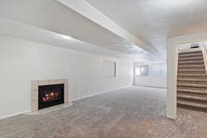Unfurnished living room featuring a tiled fireplace, carpet floors, a textured ceiling, and stairway