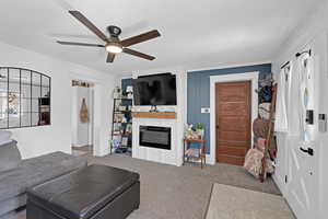 Living area with a glass covered fireplace, carpet floors, a ceiling fan, and ornamental molding
