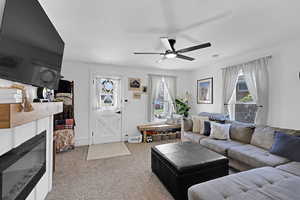 Carpeted living room featuring a glass covered fireplace, a wealth of natural light, and ceiling fan