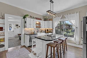 Kitchen featuring black electric cooktop, a sink, dark countertops, backsplash, and white cabinetry