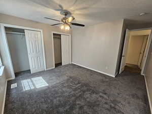 Unfurnished bedroom featuring multiple closets, dark carpet, visible vents, a textured ceiling, and ceiling fan