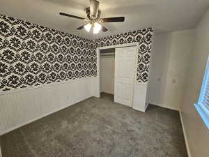 Unfurnished bedroom featuring wallpapered walls, carpet floors, a textured ceiling, and wainscoting