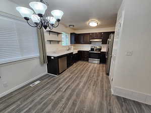 Kitchen with stainless steel appliances, open shelves, wood finished floors, a sink, and a chandelier