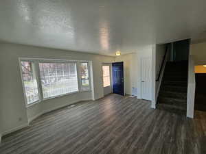 Unfurnished living room with dark wood-type flooring, stairway, a textured ceiling, and baseboards