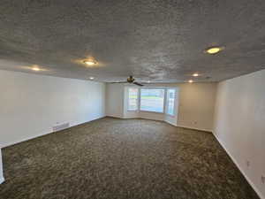 Empty room with visible vents, baseboards, a textured ceiling, carpet flooring, and ceiling fan