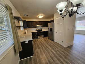 Kitchen with light countertops, a sink, baseboards, appliances with stainless steel finishes, and dark wood-style flooring