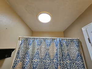 Bathroom featuring a textured wall and a shower with curtain with a sky light