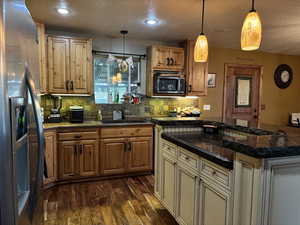 Kitchen with dark wood finished floors, stainless steel appliances, a sink, decorative backsplash, and a textured ceiling