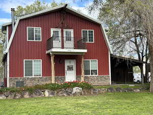 View of front facade with metal and stone siding, a balcony, and a front yard