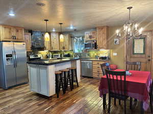 Kitchen featuring a center island, dark wood-style floors, a chandelier, range hood, and appliances with stainless steel finishes and semi-formal dining room