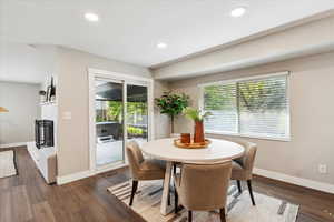 Dining area with plenty of natural light, a fireplace with raised hearth, baseboards, and dark wood-style flooring