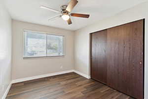 Unfurnished bedroom with ceiling fan, baseboards, dark wood-type flooring, and a closet