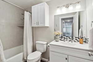 Full bathroom featuring shower / bath combination with curtain, vanity, backsplash, and toilet