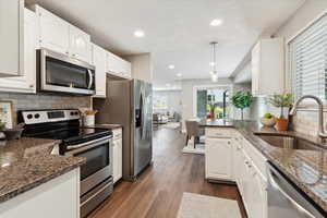 Kitchen with dark stone countertops, a sink, white cabinets, stainless steel appliances, and dark wood finished floors