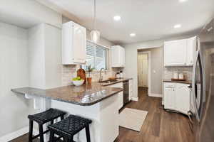 Kitchen featuring white cabinets, stainless steel appliances, a peninsula, a sink, and baseboards