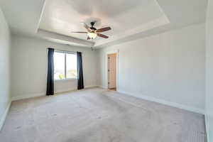 Spare room with a tray ceiling, ceiling fan, baseboards, and light carpet