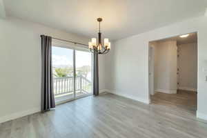 Spare room featuring baseboards, light wood-style floors, and an inviting chandelier