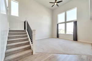 Stairway featuring ceiling fan, a high ceiling, wood finished floors, and baseboards