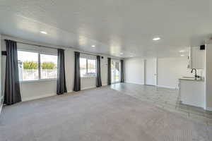 Unfurnished living room with a textured ceiling, baseboards, a sink, and recessed lighting