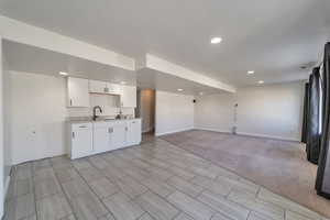 Interior space with a sink, open floor plan, baseboards, recessed lighting, and white cabinetry