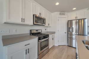 Kitchen featuring light wood finished floors, recessed lighting, white cabinetry, light countertops, and appliances with stainless steel finishes