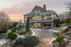 Back of property at dusk with a chimney, stairs, a patio area, stone siding, and an outdoor fire pit